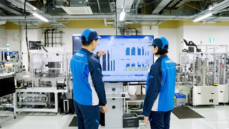 An OMRON representative reviewing data on a monitor while talking with people on the shop floor